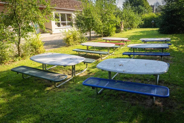 many small tables and benches stand on the lawn of a kindergarte