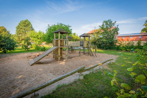 a wooden climbing frame stands on the premises of a kindergarten