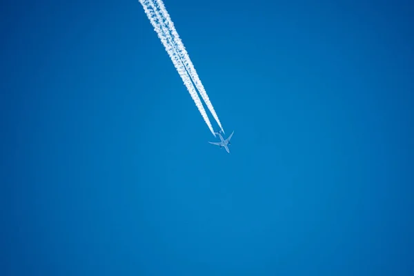 In the blue sky a big passenger plane flies and leaves behind tw — Stock Photo, Image