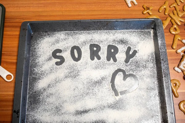 the word Sorry is written on a baking tray sprinkled with icing