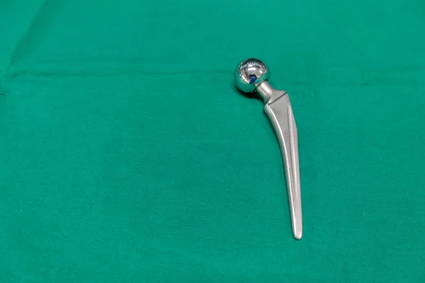 Una prótesis femoral explantada se encuentra en una cortina quirúrgica verde — Foto de Stock
