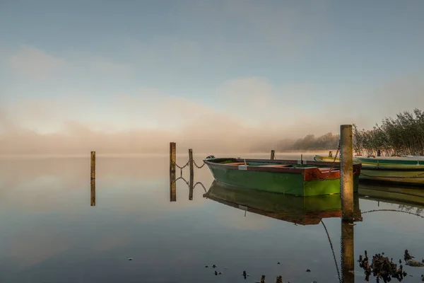 En un lago algunos botes de remos están amarrados y en el lago hay niebla — Foto de Stock