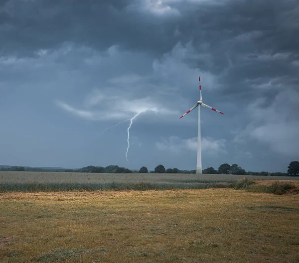 lightning strikes the ground next to a wind turbine