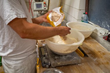 Bir fırında bir fırıncı ekmek hamuru için malzemeleri karıştırır.