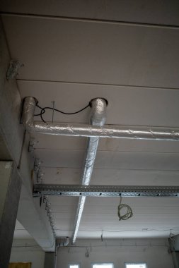 Bir inşaat alanındaki fabrika binasının tavanından dışarı bakan izole borular.  