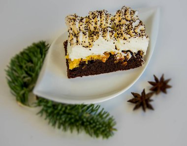 Beyaz bir üste, beyaz bir tabakta bir dilim pasta ve Noel süslemesi.