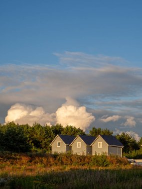 Birbirinin aynı üç küçük ahşap ev gün batımında yan yana duruyor ve gökyüzü bulutlu.