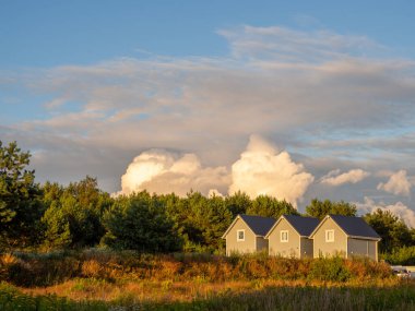 Birbirinin aynı üç küçük ahşap ev gün batımında yan yana duruyor ve gökyüzü bulutlu.