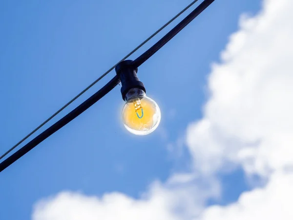 a bulb of a black chain of lights in front of a blue sky