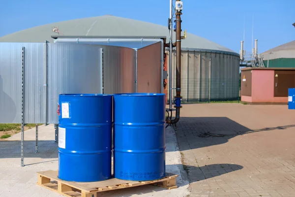 two big blue barrels stand on a wooden pallet in front of a biogas plant