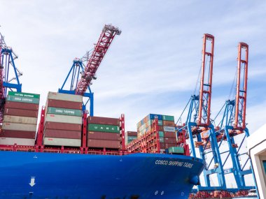 Hamburg limanında konteynırlarla dolu büyük mavi bir konteyner gemisi var.