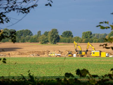 Kazıcılar ve diğer makineler büyük beton boruları gömmek için bir alanda duruyorlar.