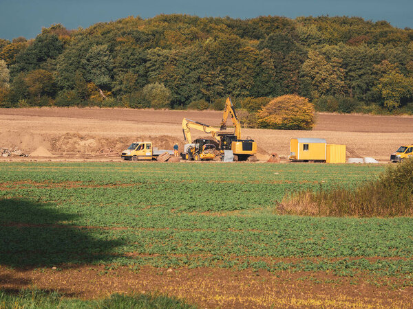 Excavators and other machines stand on a field to bury large concrete pipes