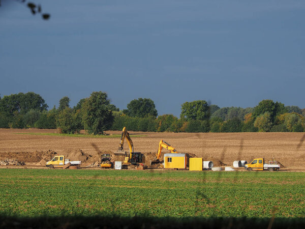Excavators and other machines stand on a field to bury large concrete pipes