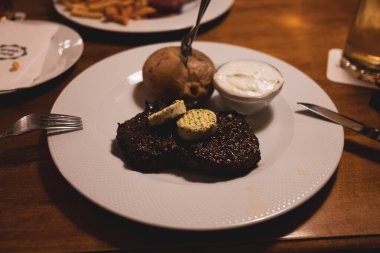 Biftek, fırında patates ve ekşi krema beyaz yuvarlak bir tabakta.