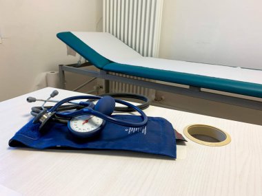 Stetoskop ve kan basıncı kelepçesi doktorun muayenehanesinin masasında ve arka planda da bir kanepe var.
