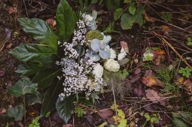Bir gübre yığınının üzerinde atılmış beyaz bir demet çiçek yatıyor.