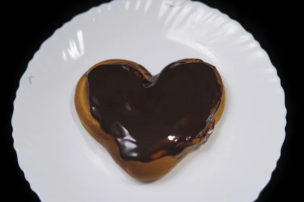 El pan en forma de corazón cubierto de chocolate, se encuentra en un plato blanco . — Foto de Stock