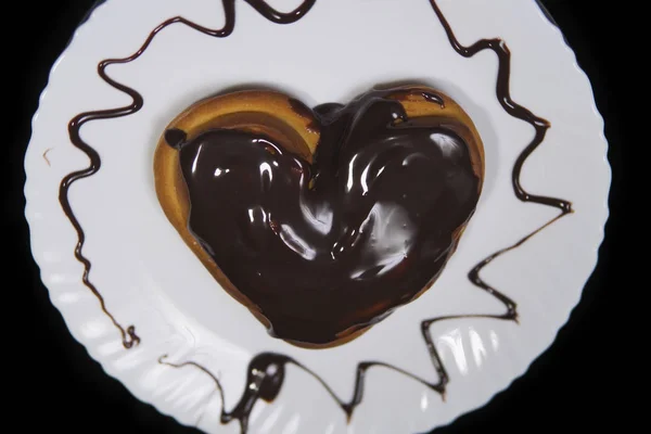 The heart-shaped bun chocolate covered, lies on a white plate. — Stock Photo, Image