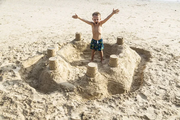 Un garçon se tient dans un château de sable — Photo