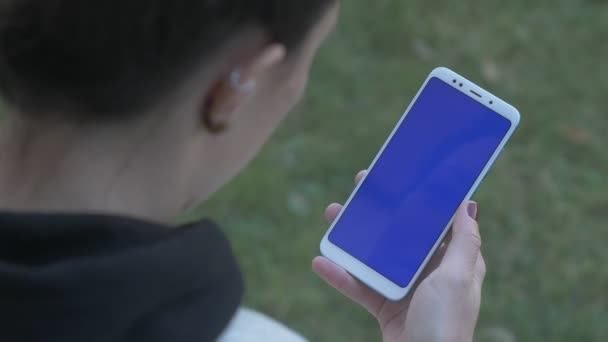 Девушка стучит и прокручивает синий экран телефона — стоковое видео