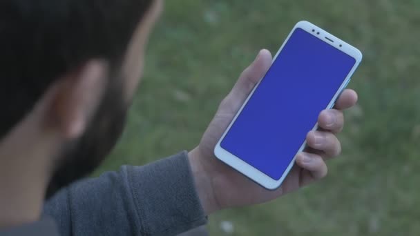 Hombre tocando en el menú en la parte inferior del teléfono de pantalla azul, por encima de la toma del hombro — Vídeos de Stock