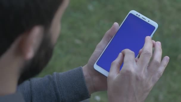 Man blauw scherm telefoon, over de schouder geschoten knijpen — Stockvideo