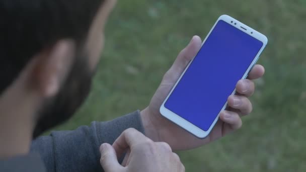 Человек стучит подержанными руками по синему экрану телефона, через плечо выстрел — стоковое видео