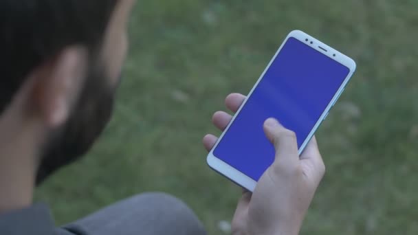 Man scrollen naar beneden op blauw scherm telefoon, over de schouder geschoten — Stockvideo