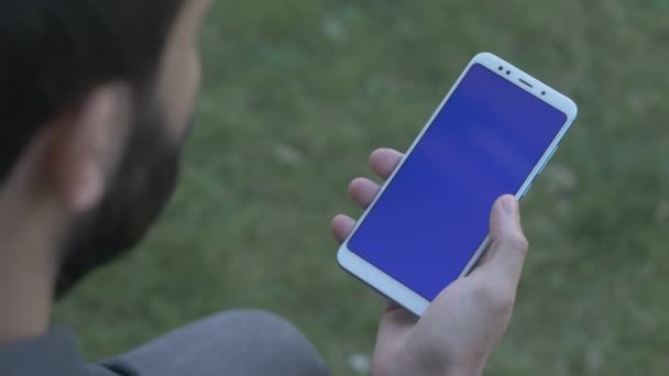 Hombre golpeando y deslizando en el teléfono de pantalla azul, por encima de la toma del hombro — Vídeos de Stock