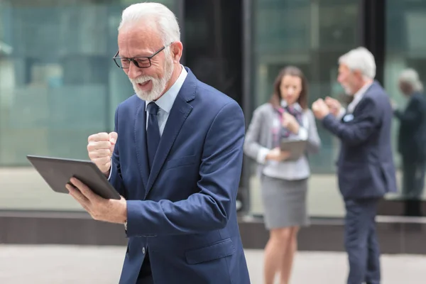 Ευτυχής ανώτερος επιχειρηματίας χρησιμοποιώντας tablet, στέκεται μπροστά από ένα κτίριο γραφείων — Φωτογραφία Αρχείου
