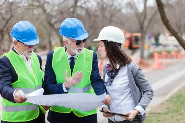 Grupo mixto de arquitectos y socios comerciales discutiendo detalles del proyecto en una obra de construcción — Foto de Stock