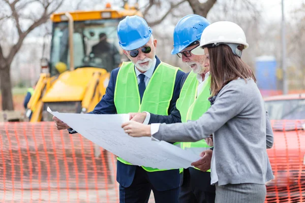 Grupo mixto de arquitectos y socios comerciales discutiendo detalles del proyecto en una obra de construcción — Foto de Stock