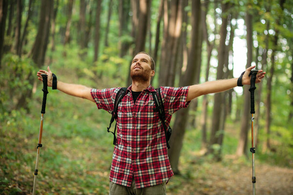 Happy young man in checkered shirt enjoying a perfect peaceful moment during hike through forest. Arms outstretched and looking into the sky. Healthy and active outdoor lifestyle