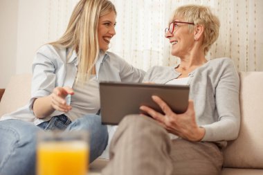 Anne ve kızı gülen ve birbirine bakarak bir tablet kullanırken