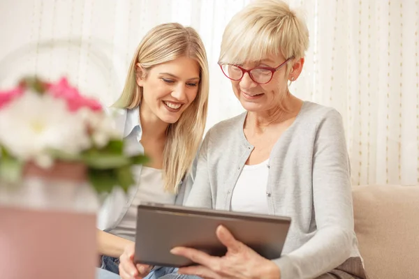 Kıdemli anne ve kızı gülümseyen ve tablet vasıl arıyorum. Çiçek buketi ön planda.