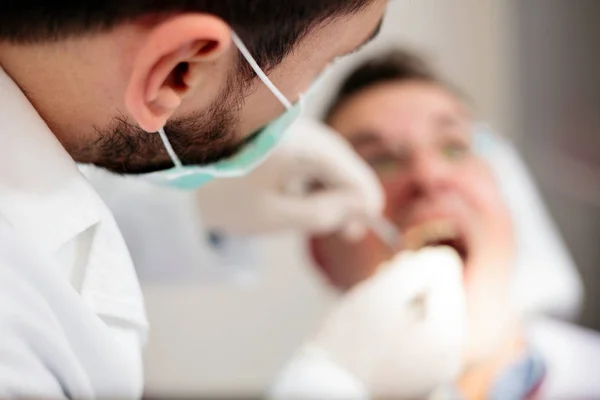 Close-up van een jonge mannelijke tandarts houden een injectiespuit, verdoving te geven aan een volwassen mannelijke patiënt. Hoge hoekmening, selectieve aandacht op voorgrond — Stockfoto