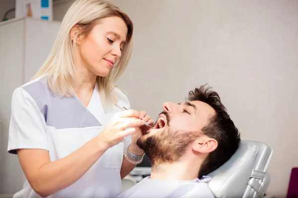 Jovem dentista examinando os dentes do paciente masculino em uma clínica odontológica — Fotografia de Stock