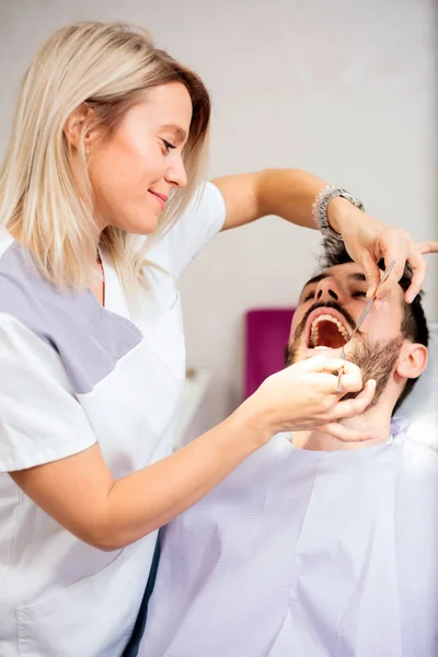 Hermosa dentista joven examinando paciente masculino joven en clínica dental —  Fotos de Stock