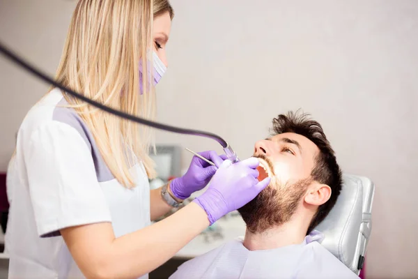 Hermosa joven dentista femenina puliendo los dientes de un joven paciente masculino en la clínica dental —  Fotos de Stock
