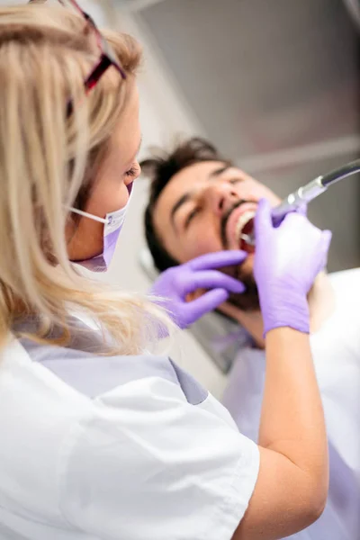 Vista de ángulo alto de una hermosa dentista joven que pule o repare la cavidad dental en los dientes del paciente masculino —  Fotos de Stock