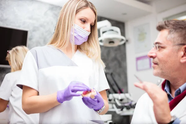 Joven mujer técnica dental consultando con un médico varón maduro en clínica dental —  Fotos de Stock