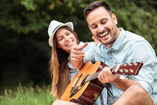 Happy young man playing guitar to his beautiful girlfriend