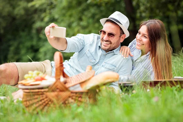 Feliz pareja joven tomando una selfie mientras disfruta de un picnic en el parque — Foto de Stock