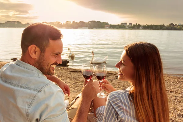 Feliz joven pareja haciendo un brindis con vino tinto. Disfrutando de picnic en la playa —  Fotos de Stock