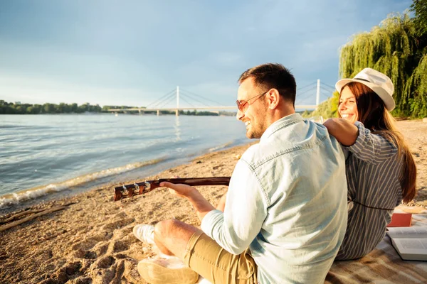 Pareja joven y feliz pasando un buen rato juntos en la playa, tocando la guitarra — Foto de Stock