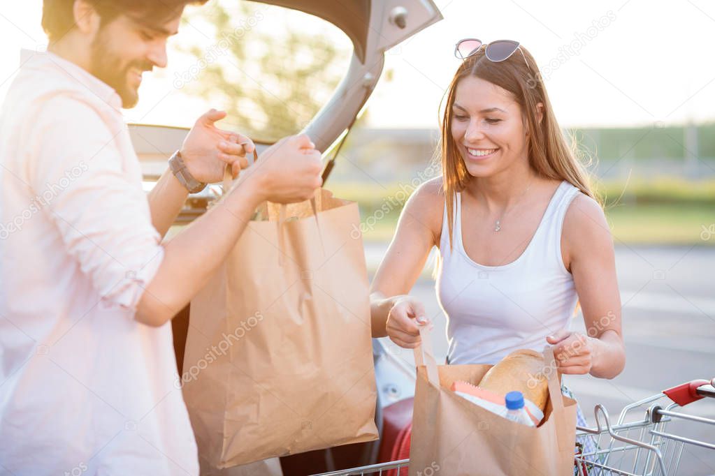 Smiling young couple unloading grocery bags from shopping cart
