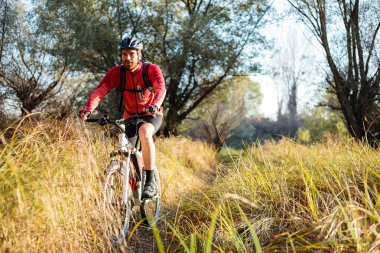 Uzun boylu çim üzerinden bir yol boyunca dağ bisikleti sürme mutlu genç sakallı adam