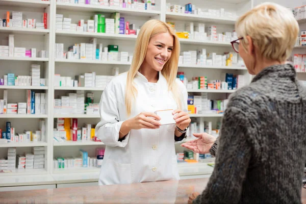 Feliz joven farmacéutico parado detrás del mostrador y sosteniendo una caja de medicamentos — Foto de Stock