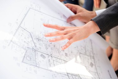 Bir inşaat yerinde meslektaşları için kat planları gösteren genç kadın mimar. Yakın çekim.